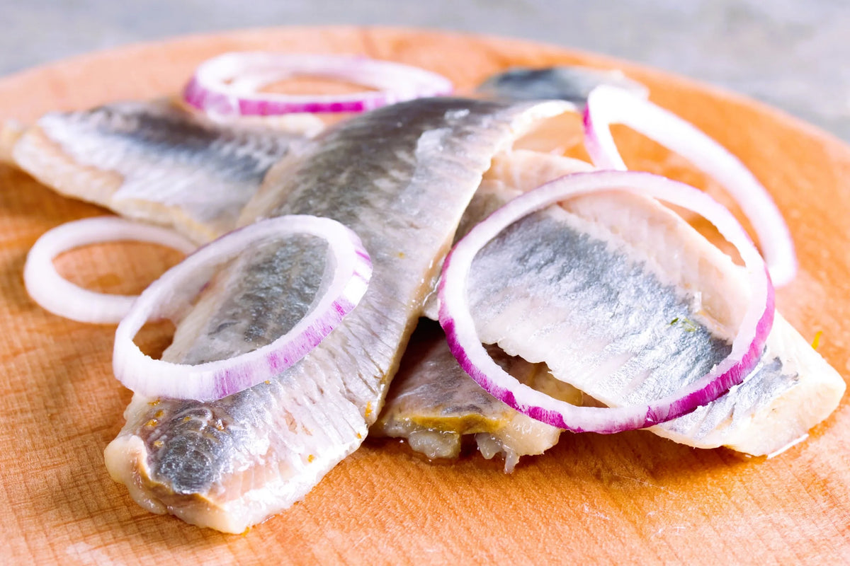 Filets de hareng tranchés avec des rondelles d'oignon rouge sur une planche à découper en bois, un plat suédois classique à base de hareng